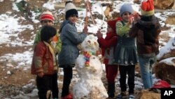 Syrian refugees children play near a snowman in a camp for Syrians who fled their country’s civil war, in the Bekaa valley, eastern Lebanon, Dec. 12, 2013. 