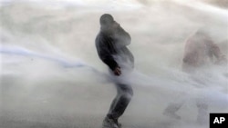 A demonstrator tries to protect himself from a police water cannon during a demonstration outside of an EU summit in Brussels, Mar 24 2011