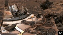 This composite image from Aug. 9, 2018 photos made available by NASA shows the Curiosity rover at Vera Rubin Ridge on Mars. A thin layer of dust is visible on the nuclear-powered rover, the result of a storm that enveloped the planet this summer.