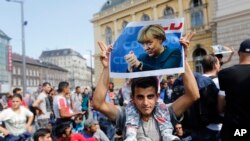 Seorang migran memegang foto Kanselir Jerman Angela Merkel sebelum memulai unjuk rasa di Budapest, Hungaria, 4 September 2015. (Foto: dok). 