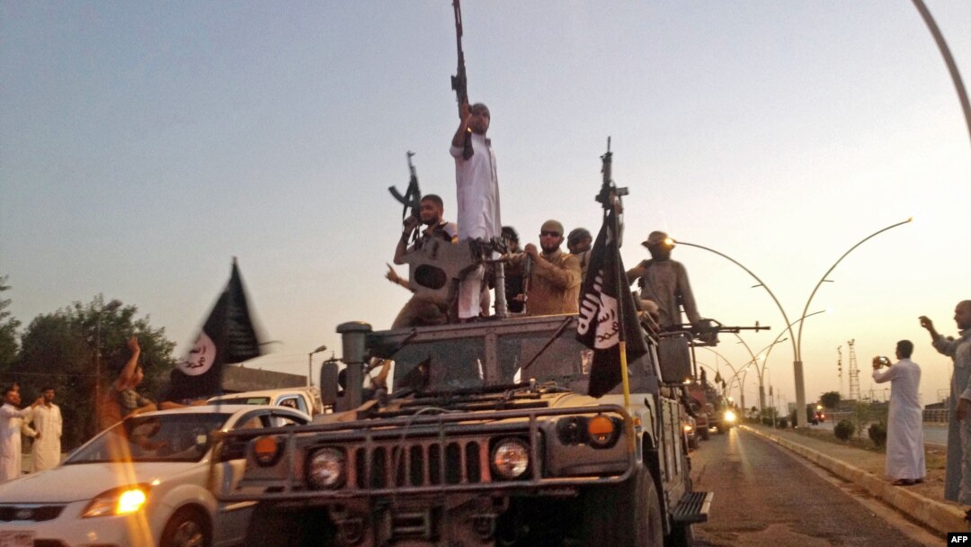 FILE - Fighters from the Islamic State group parade in a commandeered Iraqi security forces vehicle in Mosul, Iraq.