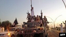 FILE - Fighters from the Islamic State group parade in a commandeered Iraqi security forces vehicle in Mosul, Iraq.