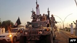 FILE - Fighters from the Islamic State group parade in a commandeered Iraqi security forces vehicle in Mosul, Iraq.