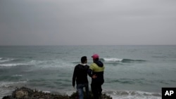 FILE - In this April 14, 2018 file photo, Ahmed Ayouby, 32, left, and Mounir Aguida, 30, who want to leave Tunisia, stand at the beach where migrants leave for Italy, in the town of Ras Jabal, Bizerte, Tunisia.