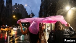 People shield themselves with a plastic rain poncho during a rainstorm in New York City, Aug. 6, 2024. 