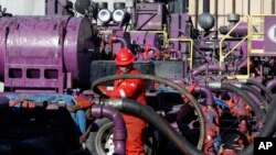 FILE - In this March 25, 2014 file photo, a worker adjusts hoses at a gas well near Mead, Colorado.