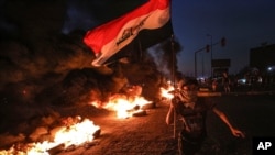 A protester runs holding an Iraqi flag as tires burn during a demonstration demanding better public services and jobs in Basra, southeast of Baghdad, Iraq, July 27, 2020. 