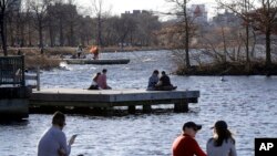 FILE - People sit on docks in the Charles River Esplanade park in Boston during unseasonably warm weather as temperatures climbed into the low 70s in areas across Massachusetts, Jan. 12, 2020. 