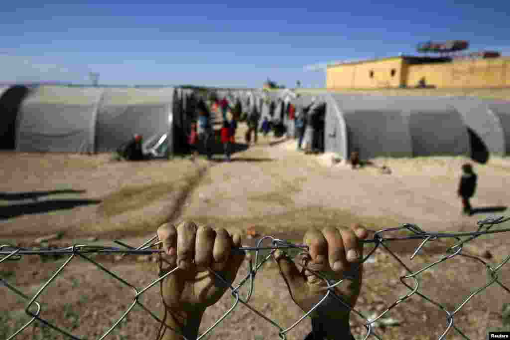 A Kurdish refugee boy from the Syrian town of Kobani holds onto a fence that surrounds a refugee camp in the border town of Suruc, Sanliurfa province, Turkey. 