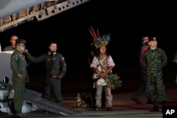 Personal militar y líderes indígenas se paran debajo de un avión después de la llegada de cuatro niños indígenas que estaban desaparecidos después de un accidente aéreo mortal, en la base aérea militar en Bogotá, Colombia, el sábado 10 de junio de 2023.(Foto AP /Iván Valencia)