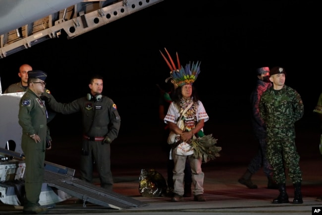 Personal militar y líderes indígenas se paran debajo de un avión después de la llegada de cuatro niños indígenas que estaban desaparecidos después de un accidente aéreo mortal, en la base aérea militar en Bogotá, Colombia, el sábado 10 de junio de 2023.(Foto AP/Iván Valencia)