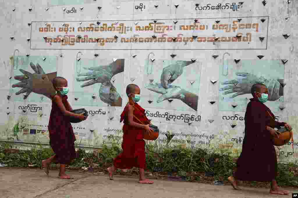 Myanmada buddist rahiblər COVID-19-la bağlı maarifləndirici posterin önündən keçirlər.&nbsp;