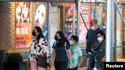 Masked people walk past posters advertising theater shows as the U.S. registers a surge in infections with the highly transmissible delta variant of the coronavirus, in New York City, July 30, 2021.