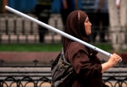 FILE PHOTO: An ethnic Uighur woman carries a metal rod as she walks down a main road in the city of Urumqi in China's Xinjiang Autonomous Region, July 10, 2019.