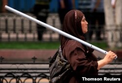 FILE PHOTO: An ethnic Uighur woman carries a metal rod as she walks down a main road in the city of Urumqi in China's Xinjiang Autonomous Region, July 10, 2019.
