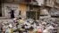 Women walk past piled up garbage after rebels took the main northern city of Aleppo and have since pushed south from their enclave in northwest Syria, Dec. 4, 2024.