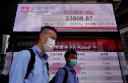 People wearing face masks walk past a bank electronic board showing the Hong Kong share index, May 5, 2020.