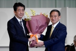 Japan's Prime Minister Shinzo Abe, left, receives flowers from Chief Cabinet Secretary Yoshihide Suga after Suga was elected as new head of Japan's ruling party at the Liberal Democratic Party's (LDP) leadership election Monday, Sept. 14, 2020, in…