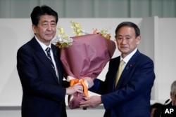 Japan's Prime Minister Shinzo Abe, left, receives flowers from Chief Cabinet Secretary Yoshihide Suga after Suga was elected as new head of Japan's ruling party at the Liberal Democratic Party's (LDP) leadership election Monday, Sept. 14, 2020, in…