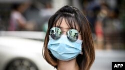 FILE - A woman wearing sunglasses and a mask to protect against the coronavirus walks on a street in Bangkok, Thailand, Feb. 13, 2020.