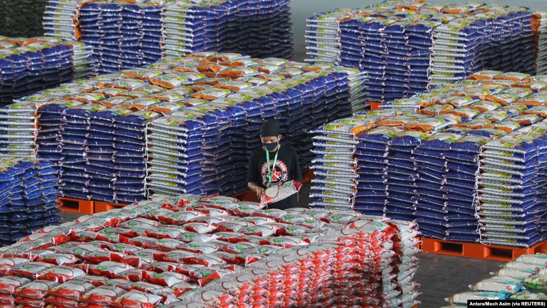 Seorang pekerja memakai masker pelindung saat menyusun tumpukan karung berisi beras, di tengah wabah Covid-19 di Surabaya, Jawa Timur, 20 April 2020. (Foto: Antara/Moch Asim via REUTERS)