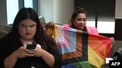 LGBTQ+ activist Waaddao Chumaporn holds a pride flag while in a waiting room with activist and representative of the marriage-equality bill Chanya Rattanatada at Thai Parliament in Bangkok on April 2, 2024, ahead of the first reading of the bill to the Senate.