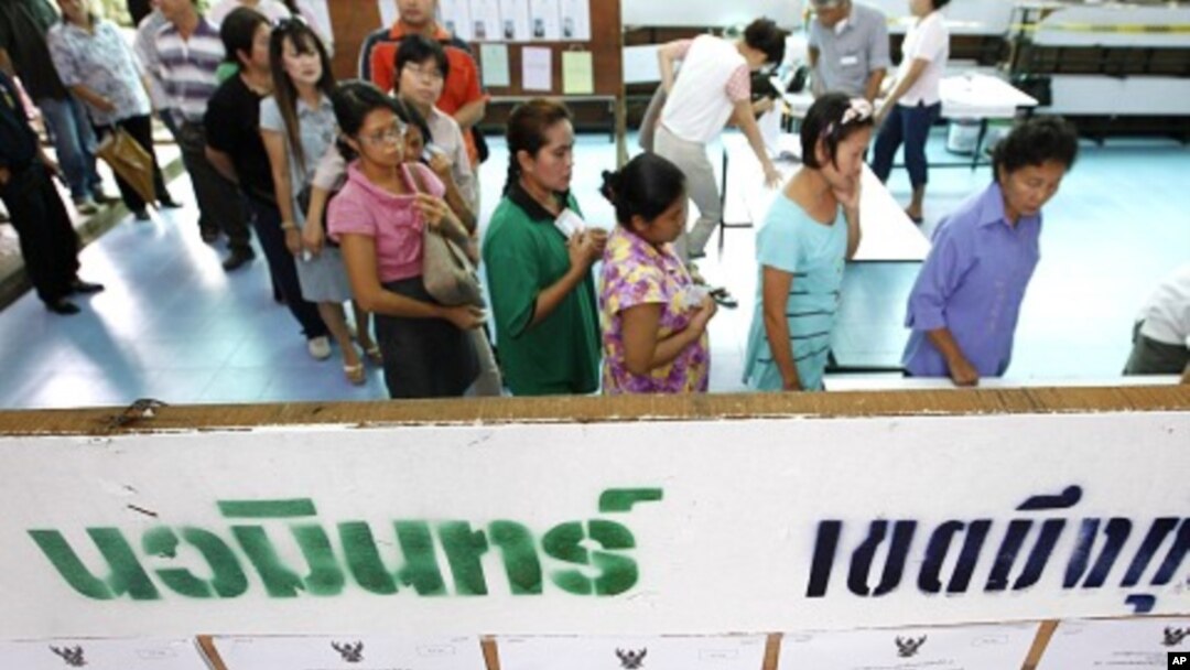 Voters wait in line to cast their votes, next to a board showing information on candidates, at a polling station in Bangkok July 3, 2011.