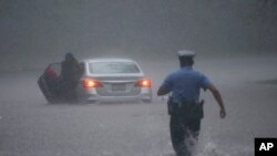 Un policier se précipite pour aider un automobiliste en détresse pendant la tempête tropicale Isaias, le mardi 4 août 2020, à Philadelphie, en Pennsylvanie. (AP Photo/Matt Slocum)