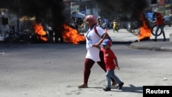 Una mujer y un niño cruzan una barricada en llamas, entre muchas más en varios vecindarios envuelto en la violencia que obliga a los residentes a refugiarse. Puerto Príncipe, Haití, el 18 de enero de 2024.