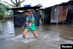 FILE - A local resident holding his daughter, walks through floodwaters after heavy rains in Malacatoya town, Nicaragua, Oct. 9, 2018.