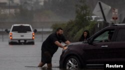 Tampak dua orang warga tengah mendorong mobil mereka yang terjebak banjir setelah badai kuat menerjang wilayah utara California di Fairfield, pada 24 Oktober 2021. (Foto: Reuters/Carlos Barria)