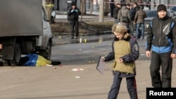 Seorang polisi berjalan di dekat korban yang ditutupi dengan bendera nasional Ukraina di lokasi serangan di Kharkiv, Ukraina timur laut, 22 Februari 2015. 