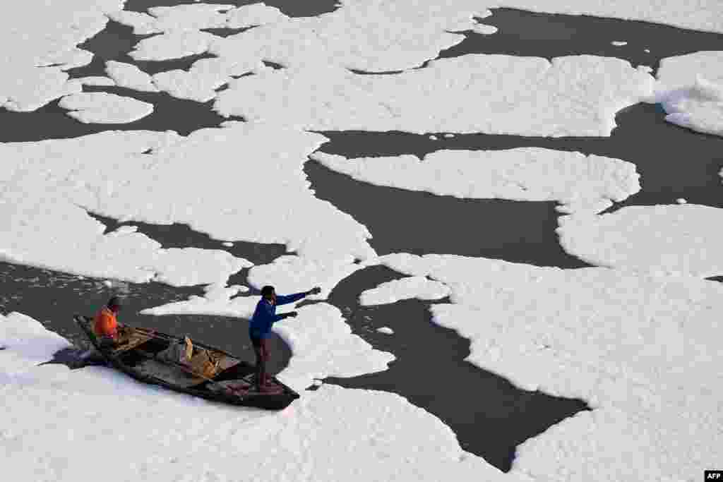 Men row a boat in the polluted waters of the Yamuna River, which is covered with foam, in New Delhi, India.