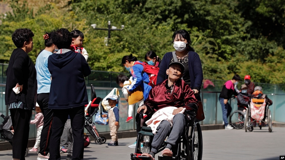 A woman pushes an elderly man in a wheelchair as residents play with their children near a commercial office building in Beijing on May 10, 2021.
