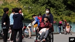 A woman pushes an elderly man in a wheelchair as residents play with their children near a commercial office building in Beijing on May 10, 2021.