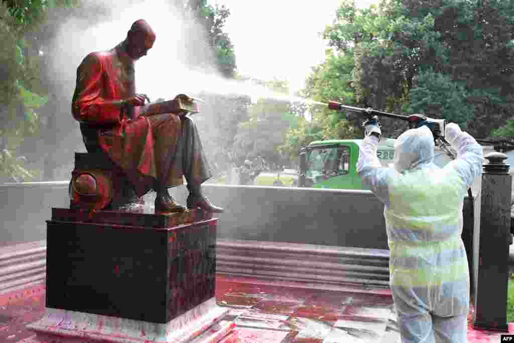 A municipal employee cleans a statue of a famous Italian journalist Indro Montanelli in a Milan public square, a day after it was defaced, stained with red paint and tagged with the inscription &quot;racist, rapist.&quot;
