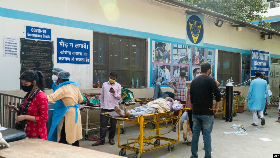Kerabat menunggu di samping pasien virus corona yang berbaring di tandu di kompleks rumah sakit untuk masuk di New Delhi, 23 April 2021. (Foto: AFP/Maude BRULARD)