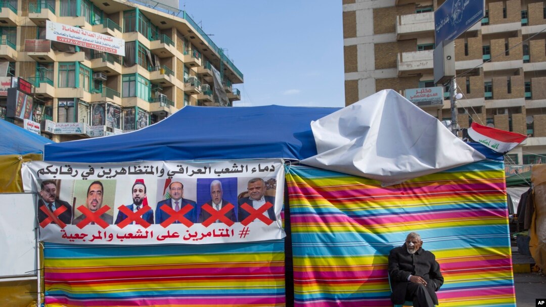 A protester sits next to a poster with defaced pictures of Iraqi politicians during ongoing protests in Tahrir square, Baghdad, Iraq, Dec. 25, 2019.