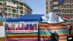 A protester sits next to a poster with defaced pictures of Iraqi politicians during ongoing protests in Tahrir square, Baghdad, Iraq, Dec. 25, 2019.