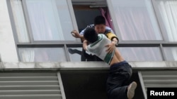 A police officer (top) grabs a man who tries to jump off the seventh floor of a hotel, in Chengdu, Sichuan province, China.