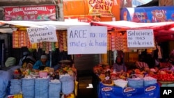 FILE - Handwritten sign with messages that read in Spanish: 'We demand solutions from the government,' 'Arce, don't starve us' and 'Solutions, not more problems' hang from vendors' stalls at a street market in La Paz, Bolivia, Oct. 21, 2024. 