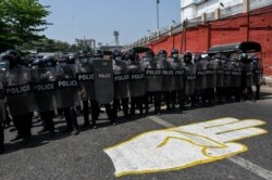 Riot police stand guard on a road, behind a street mural of the protesters' three-finger salute, after a clash between pro-junta supporters and anti-military coup protesters in Yangon, Feb. 25, 2021.