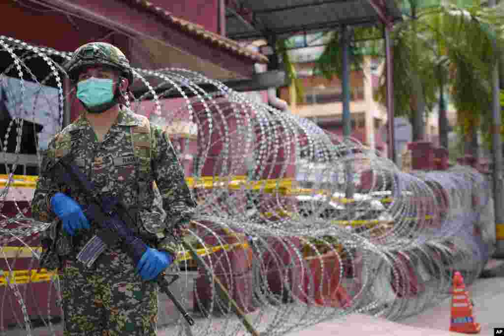 کشیدن سیم خاردار و گشت سربازان مسلح دور یک منطقه مسکونی تحت کنترل با تعداد بسیار زیاد مبتلایان به ویروس کووید – ۱۹ در حومه کوالالامپور، مالزی