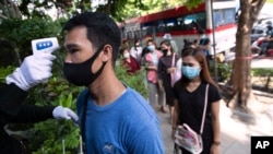 Un agente de seguridad verifica la temperatura de las personas que usan mascarillas para ayudar a frenar la propagación del coronavirus mientras hacen fila.