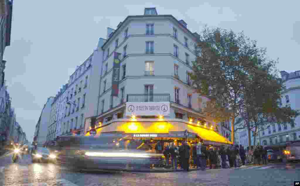 Cars pass by and people gather around La Bonne Biere cafe in Paris. The cafe where five people were killed by a squad of Islamic extremist gunmen on Nov. 13, terrorizing central Paris, reopened for business Friday.