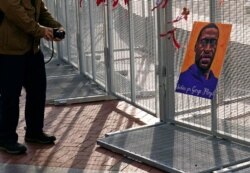 A passerby stops to take a photo of a George Floyd picture hanging on the fence surrounding the Hennepin County Government Center in Minneapolis where the trial for former Minneapolis police officer Derek Chauvin continues on April 2, 2021.