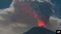 El cráter del Monte Agung brilla por la lava durante una erupción mientras arroja humo volcánico en Karangasem, isla de Bali, en Indonesia, el viernes 29 de junio de 2018. Bali cerró el viernes su aeropuerto internacional, dejando varados a miles de viajeros, cuando el volcán lanzó una columna de ceniza y humo de 2.500 metros de alto (8.200 pies). (Foto AP)