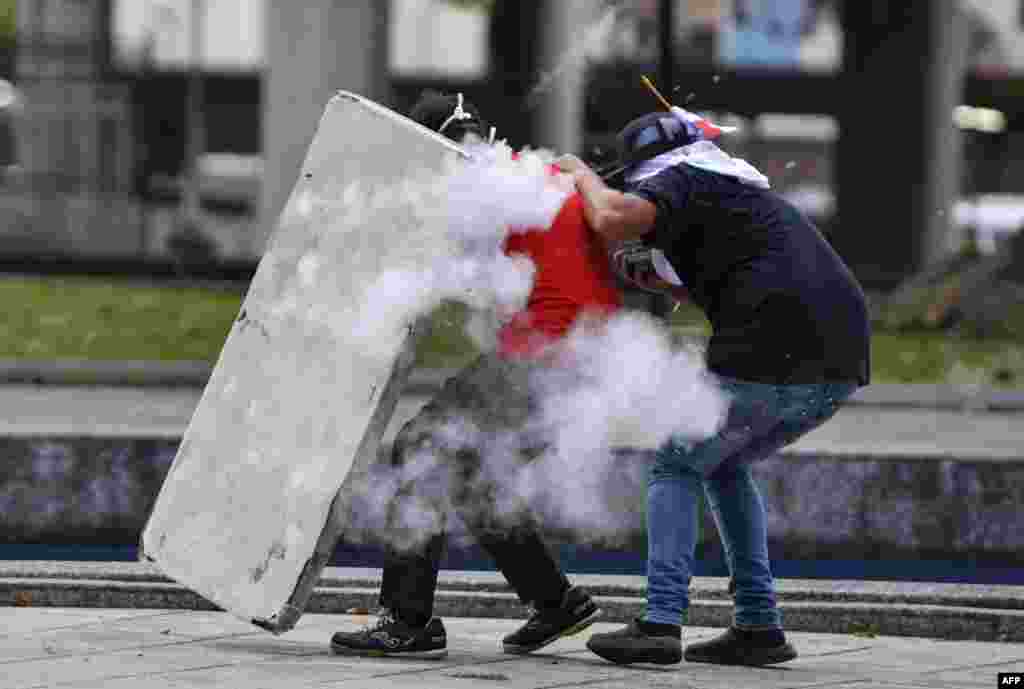 Los manifestantes se protegen mientras se enfrentan con la policía antidisturbios. 