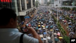 A man takes pictures as protesters wearing face masks and holding umbrellas march on a street in Hong Kong, Oct. 6, 2019.