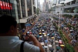 A man takes pictures as protesters wearing face masks and holding umbrellas march on a street in Hong Kong, Oct. 6, 2019.